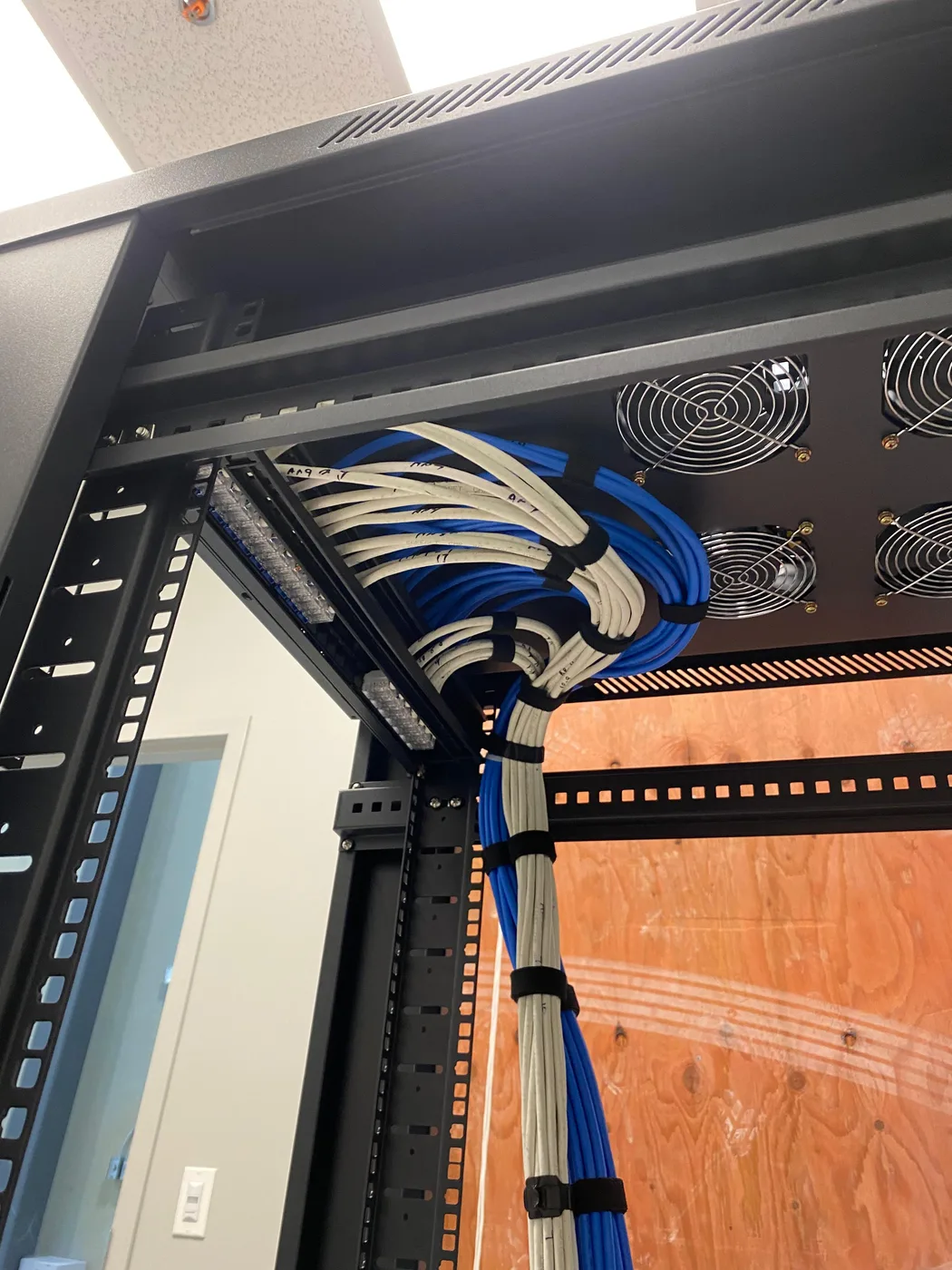 A vertical view of blue and white cable bundles entering an equipment rack and turning toward the patching area.